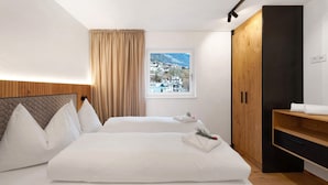 A bedroom with two beds, a window with a mountain view, a wooden wardrobe, and a small shelf with a towel. - Apartment 'Paradeis Apartments A18' with Mountain View, Private Terrace and Wi-Fi (Mühlbach)
