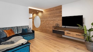 A modern living room with a sofa, a television, wooden wall paneling, and a potted plant. - Apartment 'Paradeis Apartments A18' with Mountain View, Private Terrace and Wi-Fi (Mühlbach)