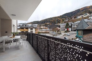 A balcony with a table and chairs, a view of a town with buildings and a hill in the background.