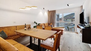 A modern living room with a wooden dining table, sofas, and a large window with a city view. - Apartment 'Paradeis Apartments A17' with Mountain View, Balcony and Wi-Fi (Mühlbach)