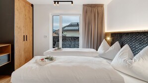 A bedroom with a large bed, a wooden wardrobe, a window with a view, and a headboard with a textured design. - Apartment 'Paradeis Apartments A17' with Mountain View, Balcony and Wi-Fi (Mühlbach)