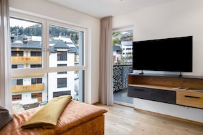A modern living room with a large window, a flat-screen TV, and a wooden bench.