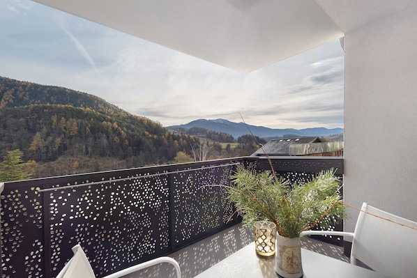 A balcony with a view of a forested mountain range, a decorative plant, and a chair.