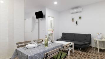 A dining area with a table set for two, a grey sofa, and a small side table with a sign.