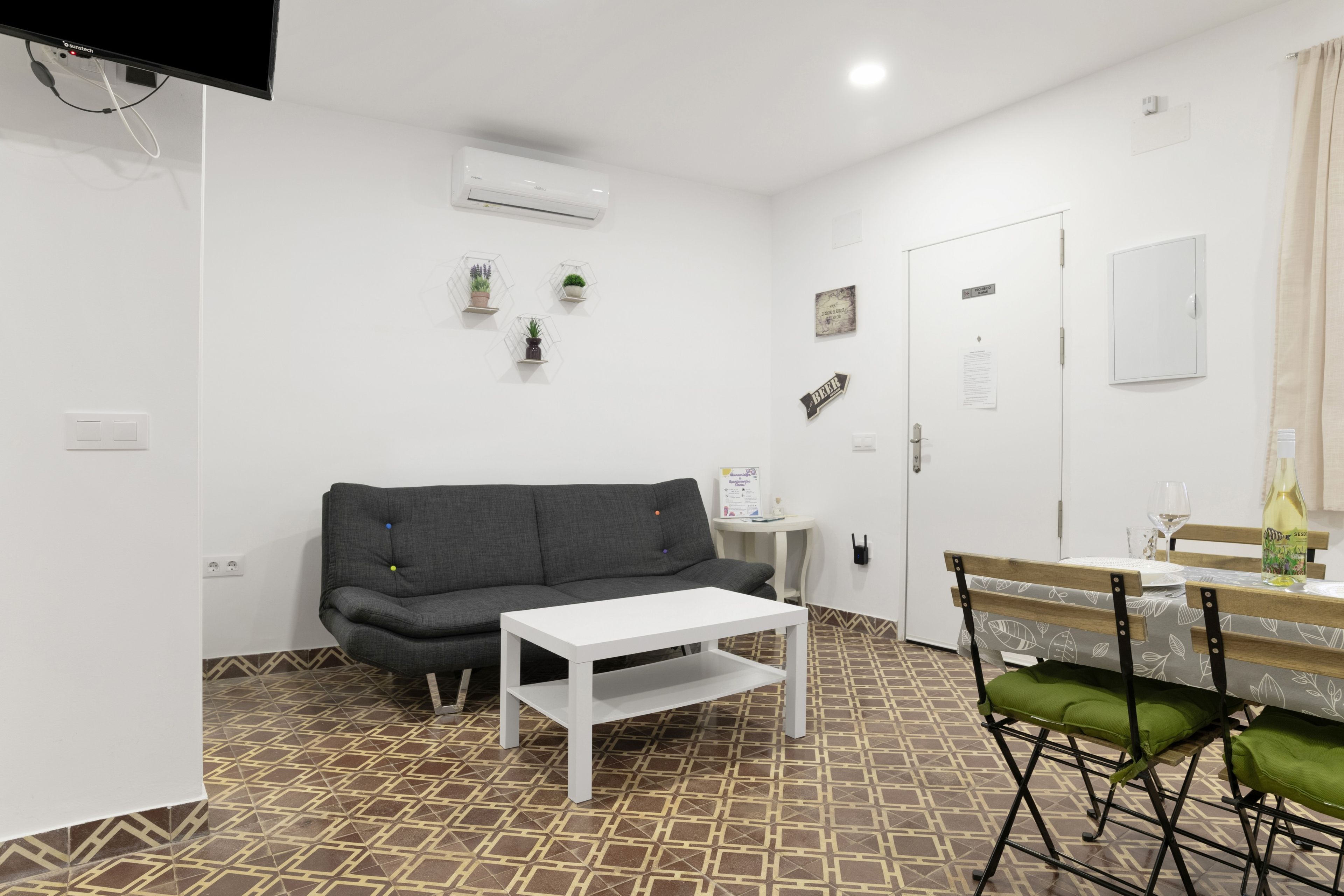 A small, modern room with a grey sofa, a white table, and a dining area with a chair.