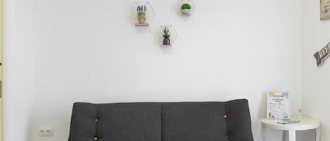 A neutral-colored sofa, a small white table, and three potted plants on a white wall.