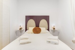 Een opgemaakt bed met twee kussens en een opgevouwen handdoek aan elke kant, een hoofdbord met een decoratief patroon en nachtlampjes op witte nachtkastjes.