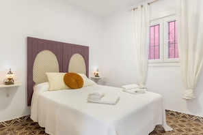 A bedroom with a bed, two bedside tables, a window with curtains, and a patterned floor.