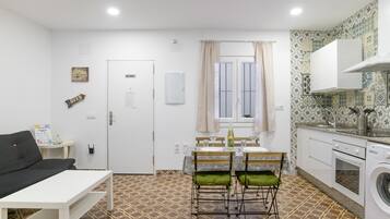 A compact living space with a kitchenette, a dining area with a table and chairs, a sofa, and a washing machine.