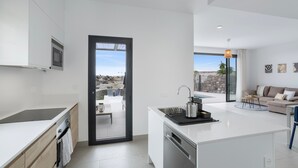 Una cocina moderna con una isla grande, lavavajillas y vistas a un patio exterior a través de una puerta abierta.
