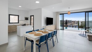 Una cocina moderna con armarios blancos, un televisor de pantalla plana y un comedor con sillas azules y una mesa blanca.