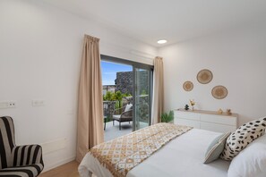 Et soveværelse med seng, stol, natbord og udsigt til en udendørs terrasse.