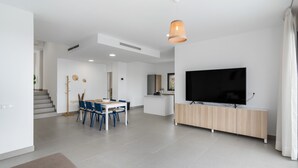 Una sala de estar moderna con comedor, televisor y una escalera que sube a otro nivel.