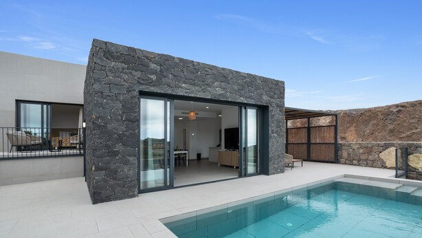Una casa moderna con piscina, fachada de piedra y amplios ventanales que dan a un interior con comedor.