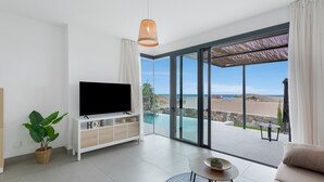 Una sala de estar moderna con un televisor de pantalla plana, un sofá, una mesa de centro y un gran ventanal que da a una zona de piscina.