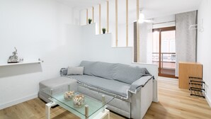 A modern living room with a glass coffee table, grey sofa, wooden beams, and a view of the outside.