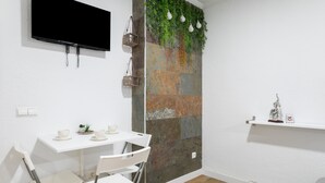 A room with a white table, two white chairs, a mounted TV, a wall with a textured pattern, and a shelf with a small statue.
