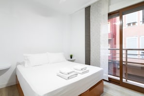 Camera d'albergo con un letto, una piccola pianta, una finestra vista edifici e una porta scorrevole.