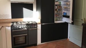 Een compacte keuken met een gasfornuis, oven en een zwarte koelkast met gedeeltelijk open deur.