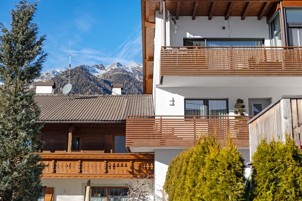 A modern building with a wooden balcony, a satellite dish, and a mountain view in the background.