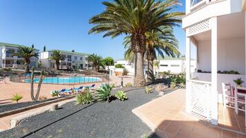 Un área de piscina con sillones de descanso, palmeras y un edificio con balcones.
