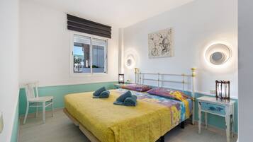 Un dormitorio con una cama, una silla, una mesita de noche, un ventanal y una lámpara fijada a la pared.