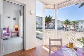 A balcony with a view of palm trees and buildings, a table with a mug, and a chair. - Holiday Apartment 'Relax Holiday' with Shared Pool, Private Terrace and Wi-Fi (Corralejo)