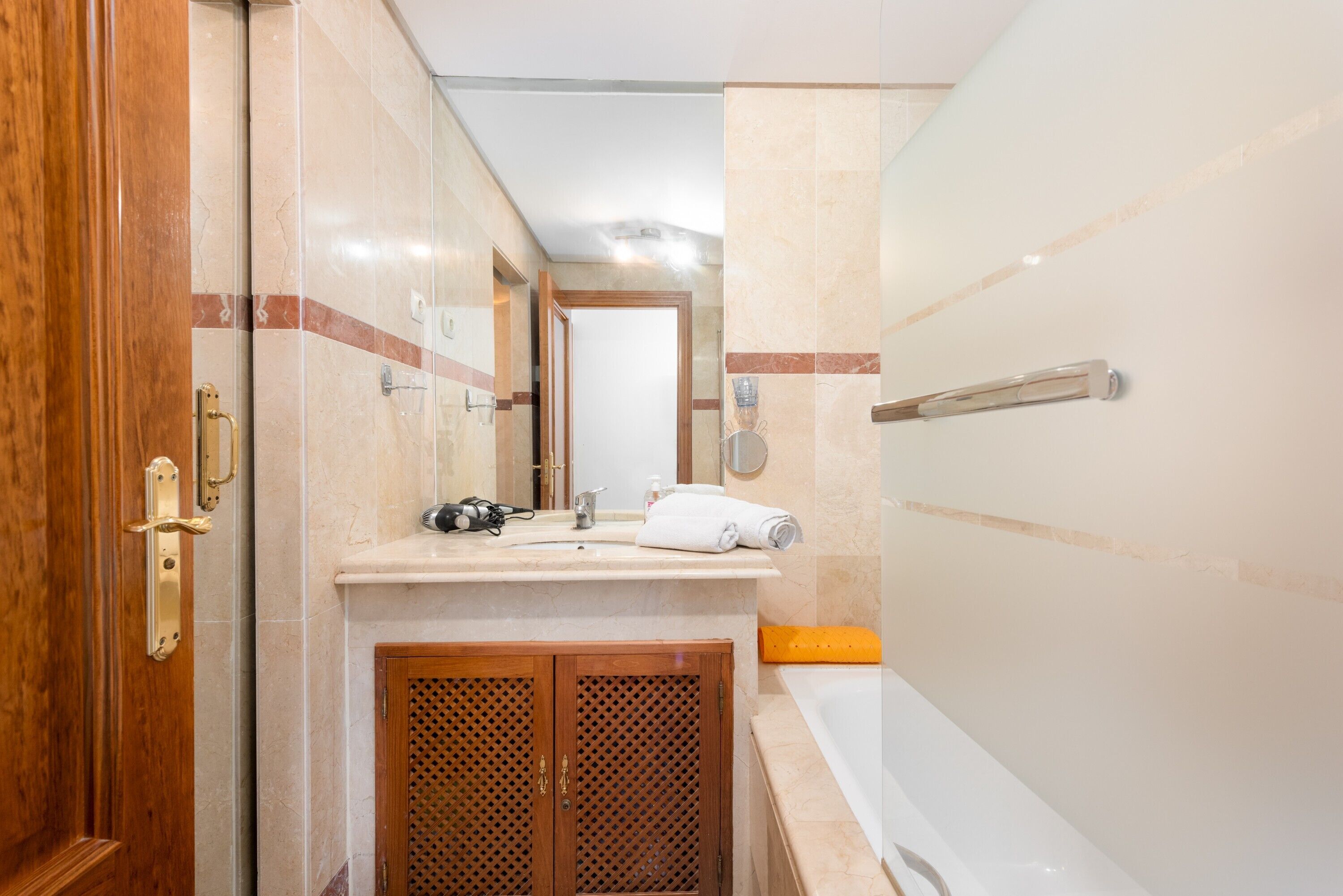 Une salle de bain avec une porte en bois, un lavabo avec un miroir, une serviette et une baignoire.