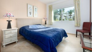 A bedroom with a bed, a nightstand, a chair, a window with curtains, and artwork on the wall. - Apartment 'Apartamento De Lujo A 30m Playa' with Sea View, Wi-Fi and Air Conditioning (Estepona)
