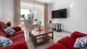 A living room with red sofas, a wooden coffee table, a TV mounted on the wall, and a view of the outdoors through a glass door. - Apartment 'Apartamento De Lujo A 30m Playa' with Sea View, Wi-Fi and Air Conditioning (Estepona)