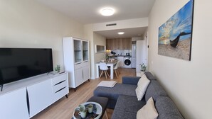 A modern living room with a flat-screen TV, grey sofa, and a dining area with a table and chairs. - Apartment 'New 3 Bed Family Suite In Mijas' with Wi-Fi and Air Conditioning (Las Lagunas de Mijas)