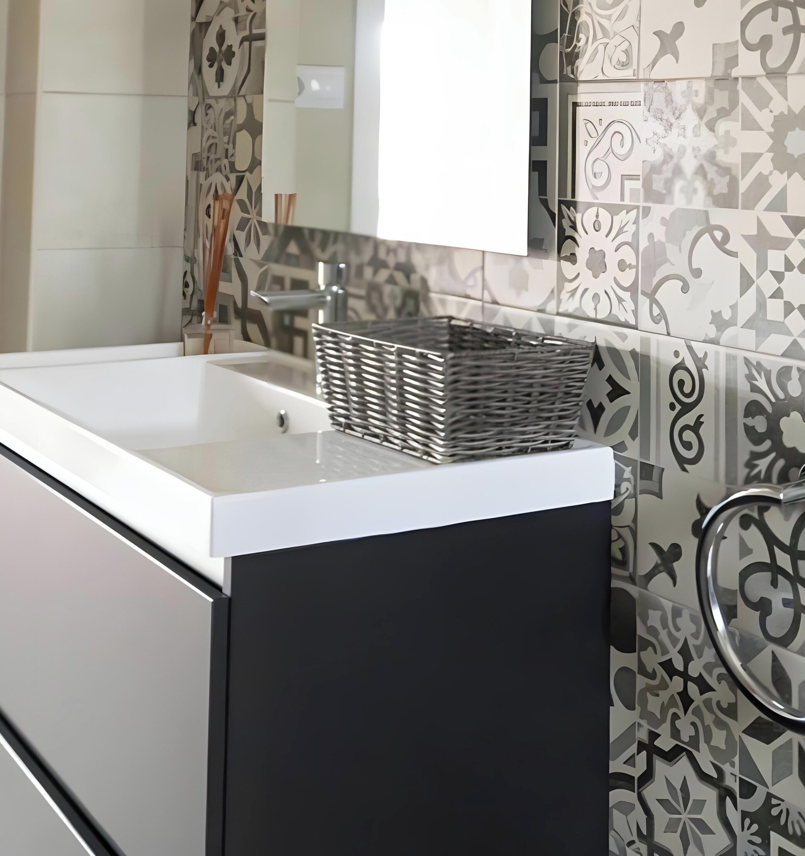 A bathroom with a white sink, a black cabinet, and patterned tiles on the walls.