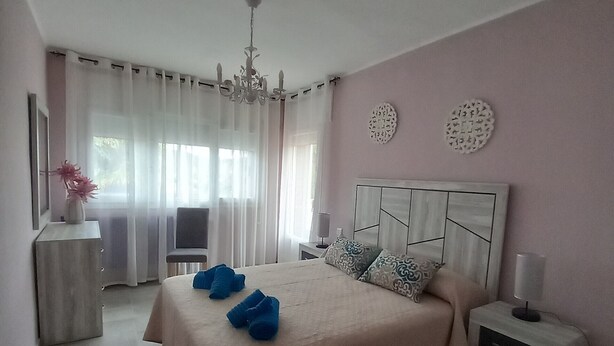 Ein Schlafzimmer mit einem Bett, Nachttischen, einem Sessel und einem Fenster mit Vorhängen.