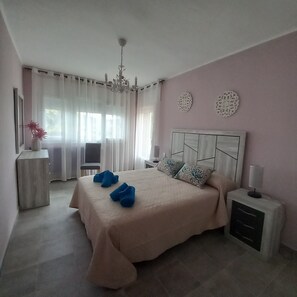 Un dormitorio con cama, mesitas de noche, una silla y una ventana con cortinas.