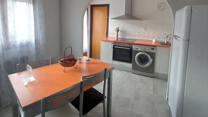Eine kleine Küche mit Esstisch, Stühlen, einer Waschmaschine und einem Kühlschrank.