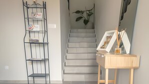Eine Treppe mit einer Pflanze auf der Zwischenebene, ein Metallregal mit Gegenständen und ein Holztisch mit Vase und Reed-Diffuser.