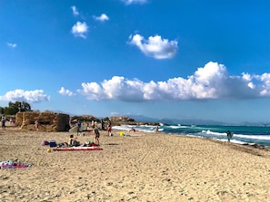 A sandy beach with people, a stone structure, and the sea.