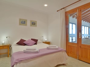 A bedroom with a bed, two bedside tables, a wooden door, and two framed pictures on the wall.