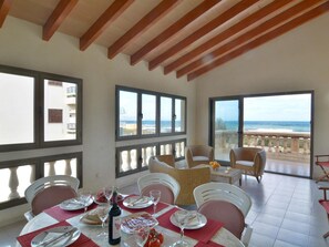 A dining area with a table set for two, large windows with ocean views, and a balcony with wicker furniture.