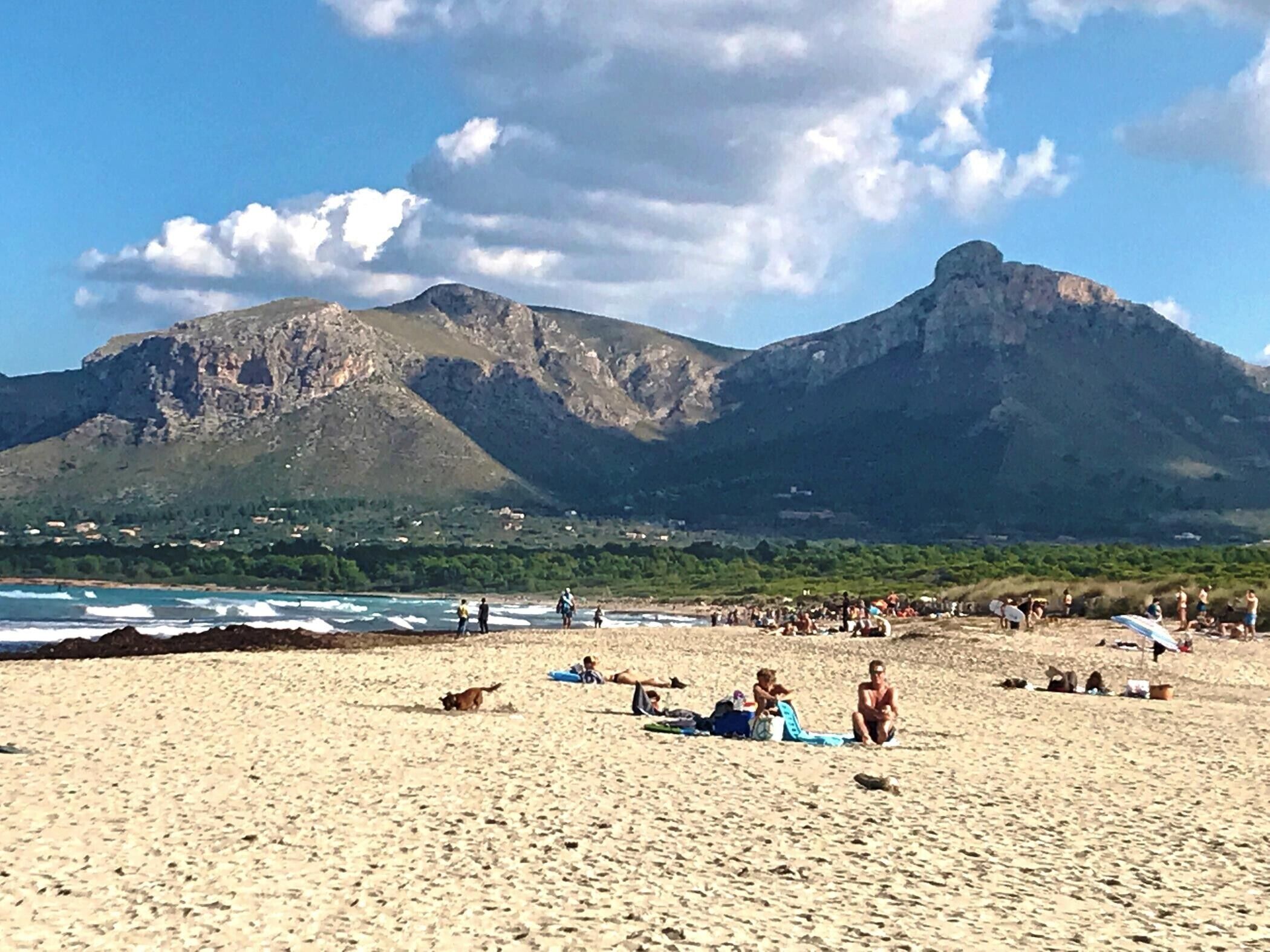 Une plage avec des gens, des montagnes et un ciel dégagé.