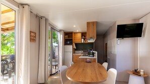 A modern kitchen with a wooden table and chairs, a built-in oven, and a TV mounted on the wall. - Mobile Home 'Camping Lou Soulei 218' with Sea View, Shared Pool and Air Conditioning (Carry-le-Rouet)
