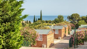 A row of wooden cabins with a view of the sea, surrounded by greenery and flowering plants. - Mobile Home 'Camping Lou Soulei 218' with Sea View, Shared Pool and Air Conditioning (Carry-le-Rouet)