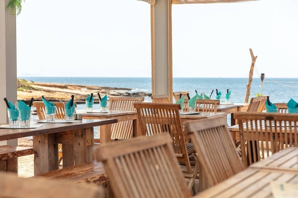 A seaside restaurant with wooden tables and chairs, arranged for dining with a view of the ocean.