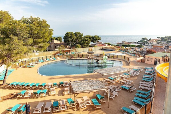 A resort pool area with sun loungers, a central pool, and a view of the sea.