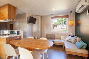 A compact living space with a kitchenette, a dining area, a sofa, and a window providing a view of the outdoors.