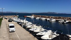 A marina with boats docked, a parking area with a white van, and a clear view of the water and distant mountains. - Beautiful Front-Line Beach House in Mallorca (Son Serra de Marina)