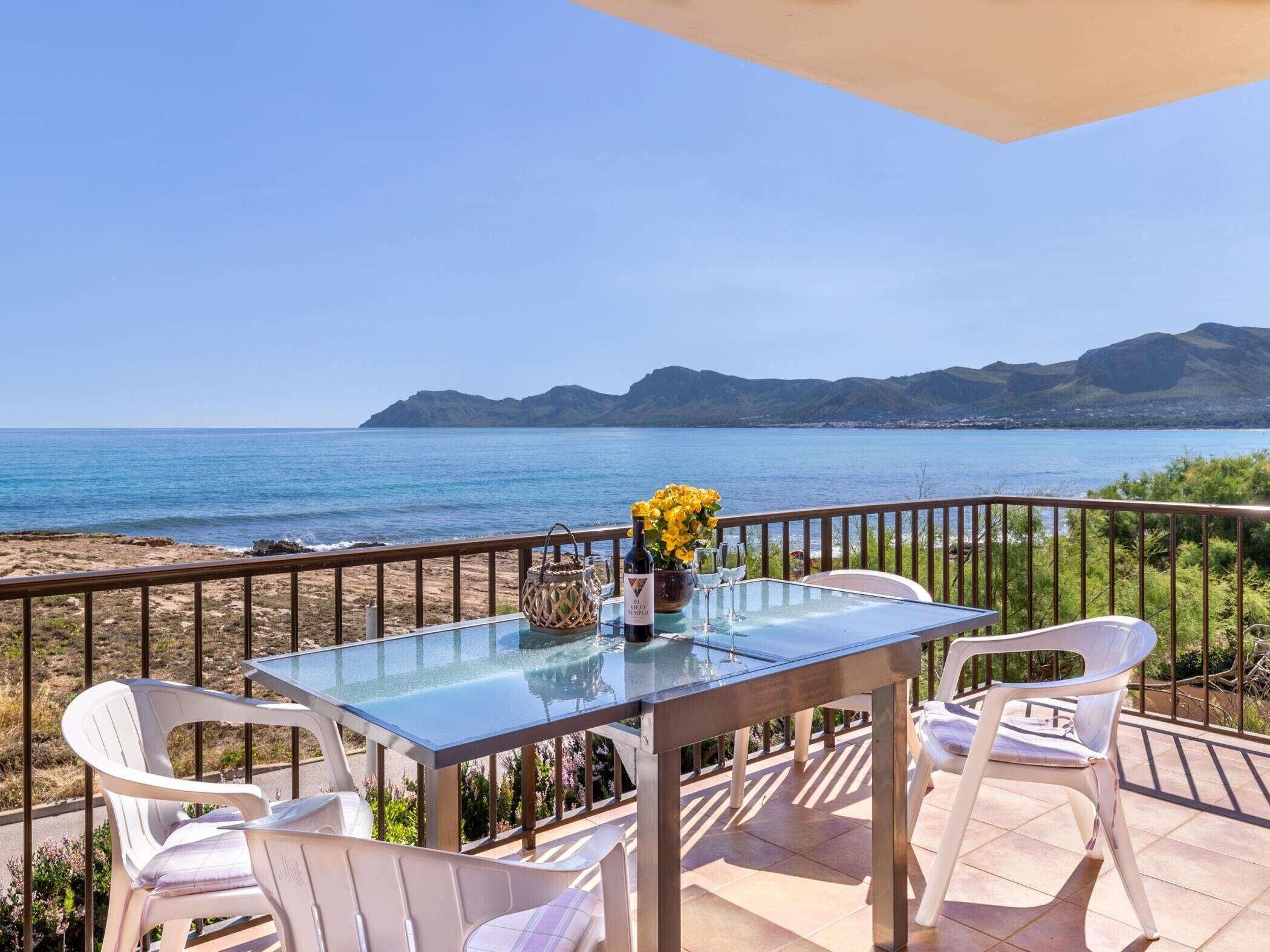 Ein Tisch mit Glasplatte und Stühlen auf einem Balkon mit Blick aufs Meer.
