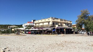 A beachfront area with buildings, outdoor seating, and a sandy foreground. - Beautiful Front-Line Beach House in Mallorca (Son Serra de Marina)