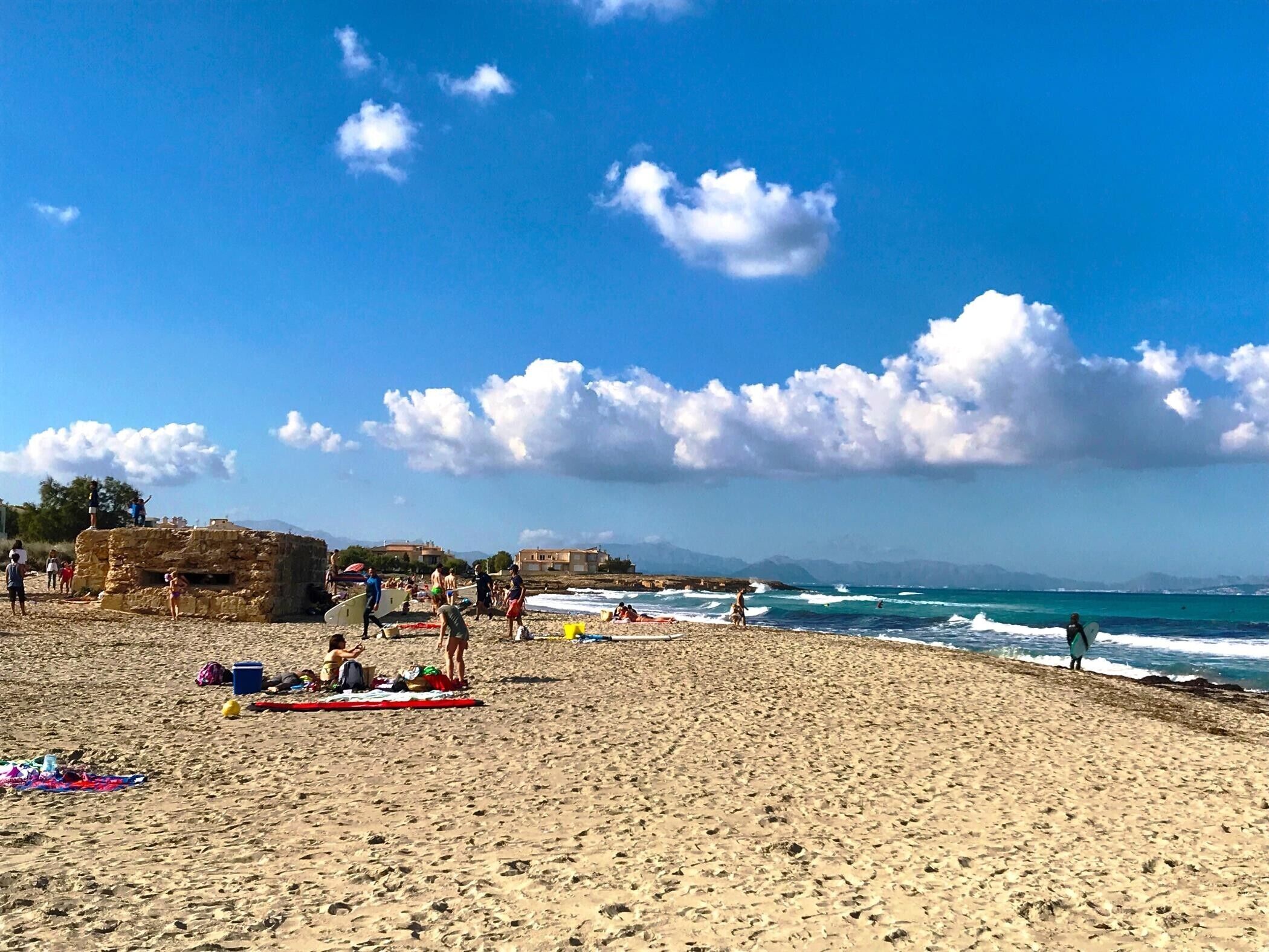 A sandy beach with people, a stone structure, and the sea.