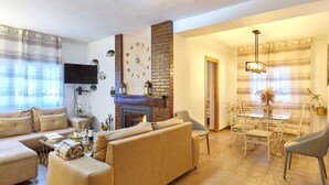A living room with a sofa, a fireplace, a TV, and a dining area with chairs and a table.